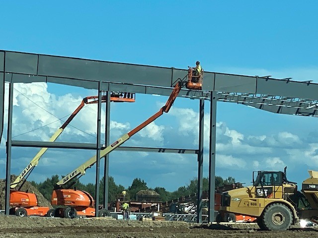 Close up of workers in raised hydraulic platforms securing steel grids at top to the sides of the steel framework structure